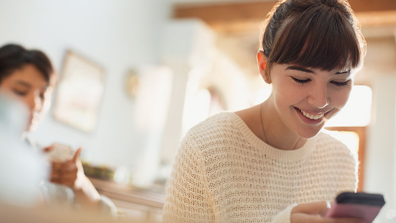 A woman smiles as she checks her phone, satisfied with the secure online checkout process. 