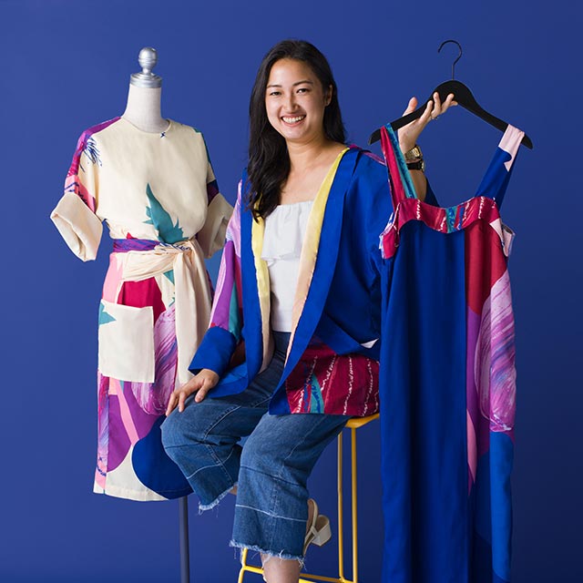 A woman posing next to a dress while seated on a chair, advertising an ecommerce starter kit for fashion entrepreneurs. 