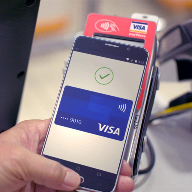 A Visa card displayed on a smartphone held by a person, utilizing mobile contactless payments for fast and secure transactions. 